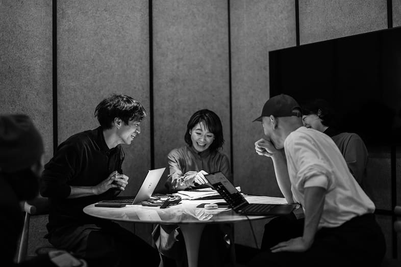 モノクロで撮影されたウェディングプランニングミーティング｜ノートパソコンを囲むクリエイティブチーム