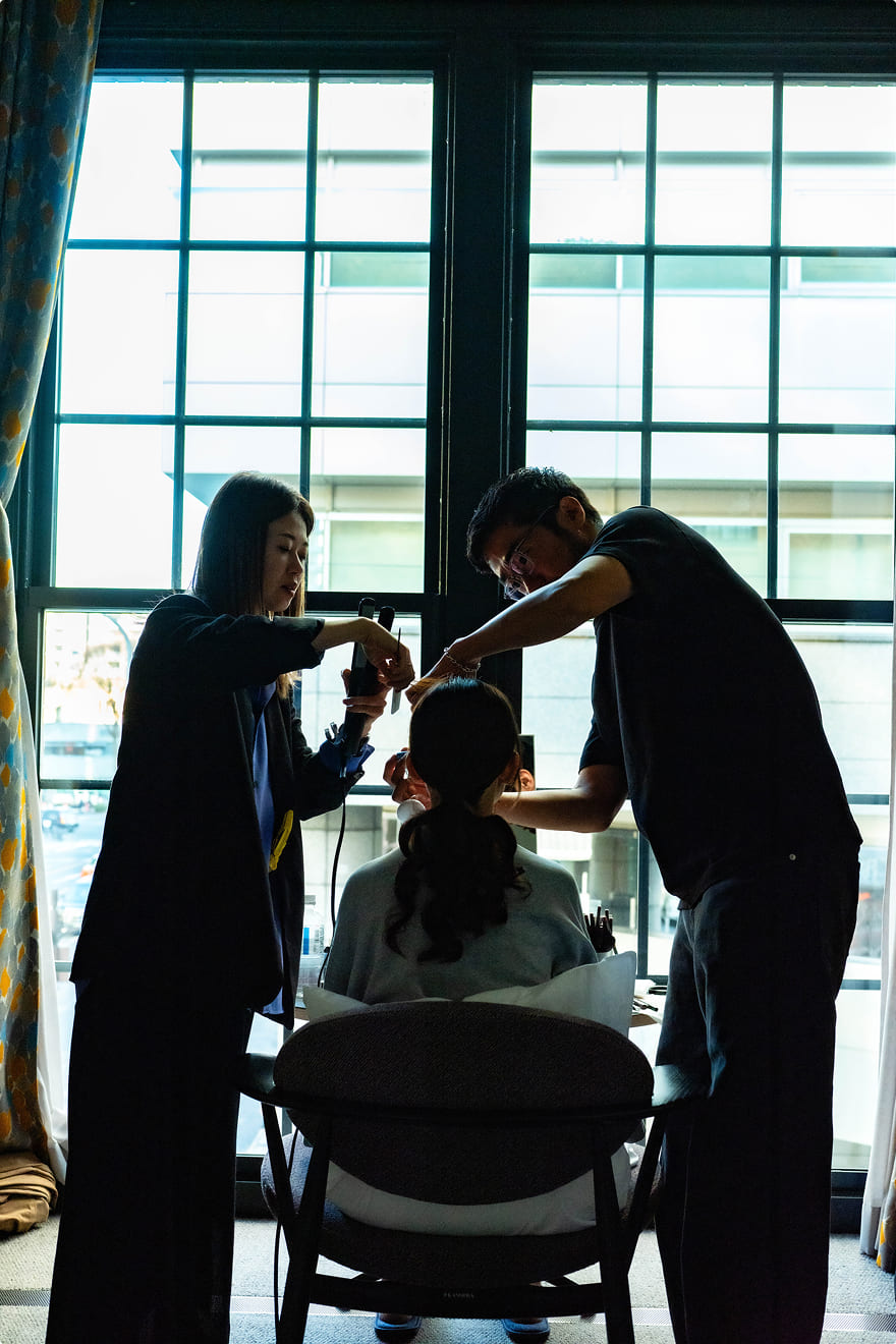 窓辺でヘアメイクを施される花嫁のシルエット|エースホテル京都ブライダル準備